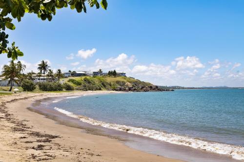 a beach with a house on a hill next to the ocean at Cooee Bay Beach House in Yeppoon