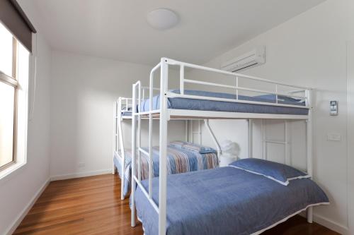 two bunk beds in a white room with wood floors at Amaroo in Queenscliff