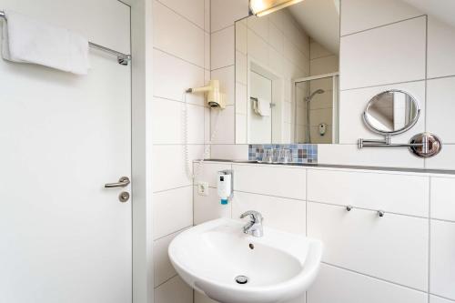 a white bathroom with a sink and a mirror at Dorint Parkhotel Siegen in Siegen