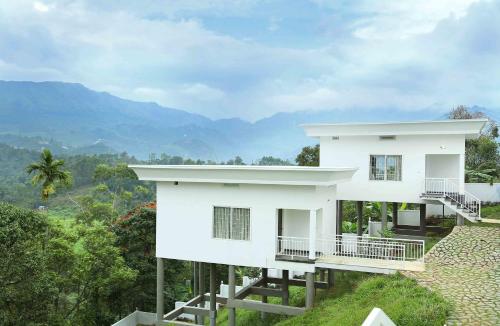 a white house on a hill with mountains in the background at The Fog Munnar (Resort & Spa) in Munnar