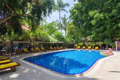 a pool at a resort with yellow chairs and trees at Tropica Bungalow Beach Hotel in Patong Beach