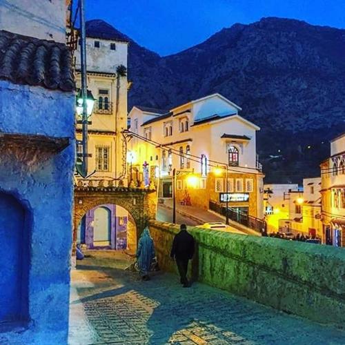 a man walking down a street in a city at night at Casa Plasa Grande CHEFCHAOUEN in Chefchaouene