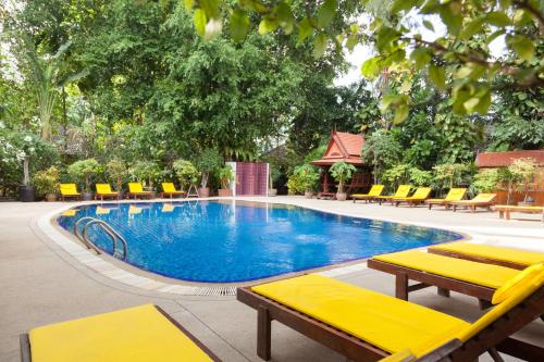 a swimming pool with yellow lounge chairs and trees at Tropica Bungalow Beach Hotel in Patong Beach