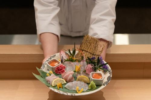 a person holding a plate of food on a table at Arima Onsen ShikinoIrodori Hatago in Kobe