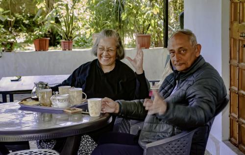 a man and woman sitting at a table with their hands up at Tranquility homestay in Shivpurī