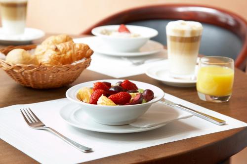 a table with plates of food and a bowl of fruit at Hotel Baseler Hof in Hamburg