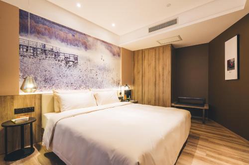 a bedroom with a white bed and a painting on the wall at Atour Hotel Hongqiao Hub National Exhibition Center Shanghai in Shanghai