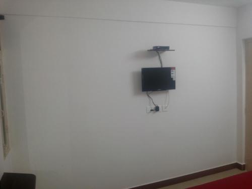 a room with a white wall with a tv on it at Hotel Nambi in Madurai