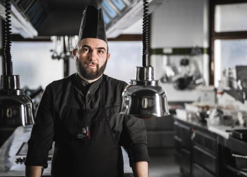 um homem usando um chapéu de chef de pé em uma cozinha em Boutique & Gourmet Hotel Orso Grigio em San Candido