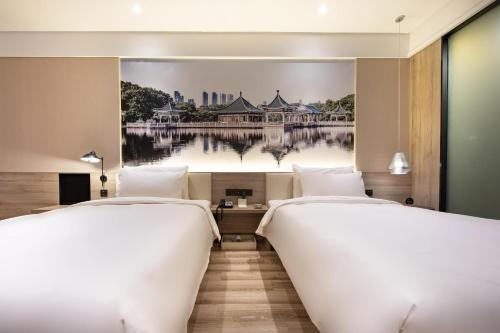 two beds in a hotel room with a painting on the wall at Atour Hotel Wuhan Tianhe Airport Tenglong Avenue Subway Station in Wuhan