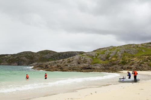 a group of people standing in the water on a beach at Achmelvich Beach Youth Hostel in Achmelvich