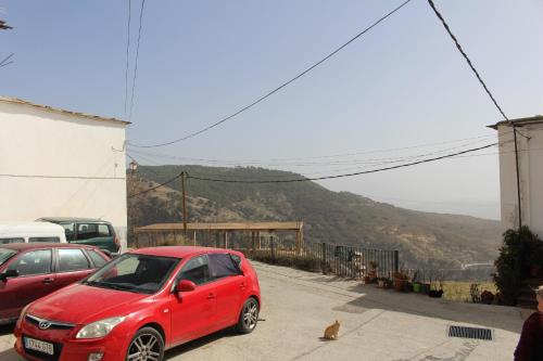 a red car parked in a parking lot with a cat at Casa Estrella de las nieves La Alpujarra in Bérchules