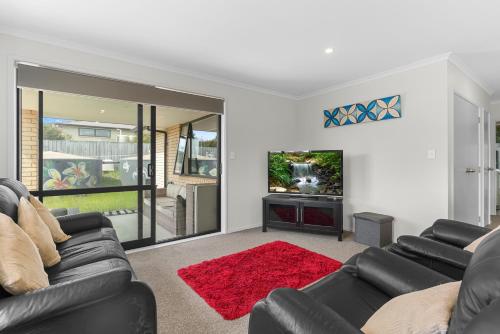 a living room with a couch and a tv at Summertime Bliss - Mangawhai Heads Holiday Home in Mangawhai