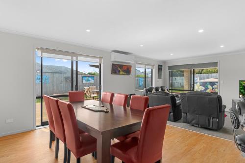 a dining room with a table and red chairs at Summertime Bliss - Mangawhai Heads Holiday Home in Mangawhai