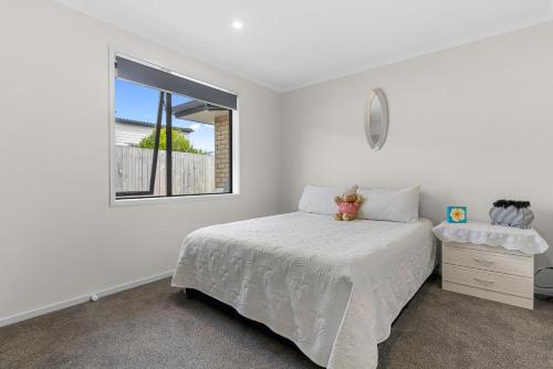 a white bedroom with a bed and a window at Summertime Bliss - Mangawhai Heads Holiday Home in Mangawhai