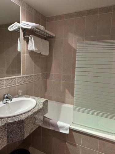a bathroom with a sink and a bath tub with a mirror at Hôtel et Restaurant Domaine de l'Orangerie in Bonnat