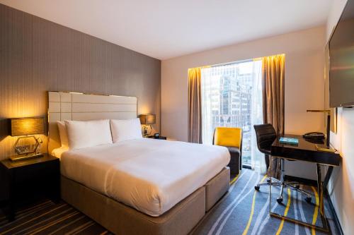 a hotel room with a bed and a desk and a window at Leonardo Hotel London Aldgate - formerly Hotel Saint in London