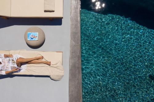 a woman laying on a bed next to a swimming pool at Madame Kalitsi Cozy Suites in Fira