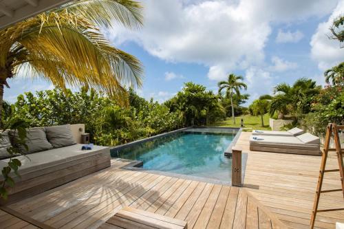 un patio trasero con piscina y terraza de madera en Villa La Vanille à Marie Galante - vue mer & piscine, en Grand-Bourg