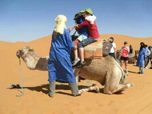 two children riding on the back of a camel in the desert at Khadija Desert Camp in Merzouga