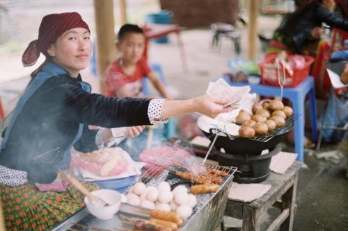 a woman is cooking food in a market at Rainbow House Ha Giang in Ha Giang