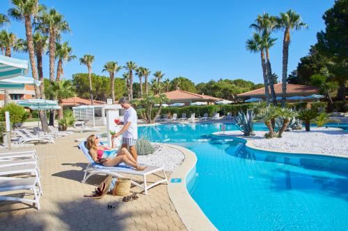 a man and a woman sitting on chairs next to a swimming pool at The Signature Level at Grand Palladium Sicilia Resort & Spa in Campofelice di Roccella