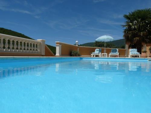 une grande piscine bleue avec 2 chaises et un parasol dans l'établissement Domaine de Coussères, à Saint-Paul-de-Fenouillet