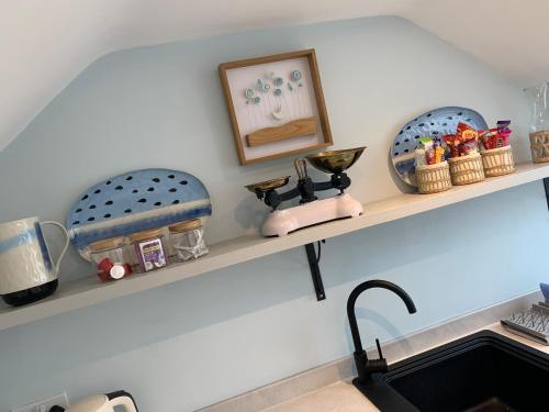 a shelf above a kitchen counter with dishes and a sink at The Seawitch - harbourside apartment in Mousehole