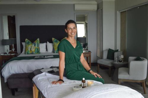 une femme assise sur un lit dans une chambre d'hôtel dans l'établissement African Oceans Manor on the Beach, à Mossel Bay