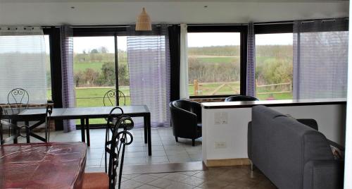 a living room with a table and chairs and windows at Gîtes Bellevue et Mascaret in Courtils