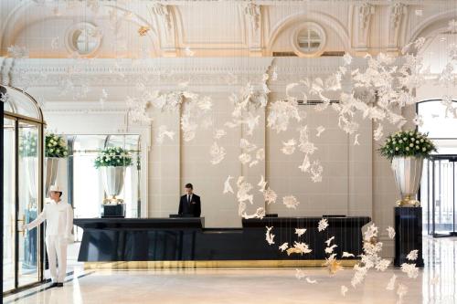 a man in a white suit standing in a lobby with a counter at Hotel The Peninsula Paris in Paris