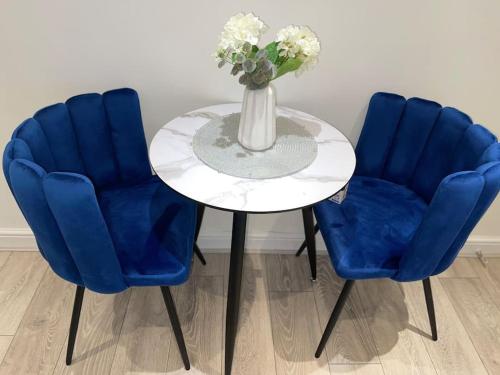 stół z 2 niebieskimi krzesłami i wazon z kwiatami w obiekcie Stylish Cosy Studio Apartment w mieście Kent