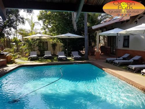 a swimming pool with chairs and umbrellas next to a house at Ocean Park Guest House in Umkomaas