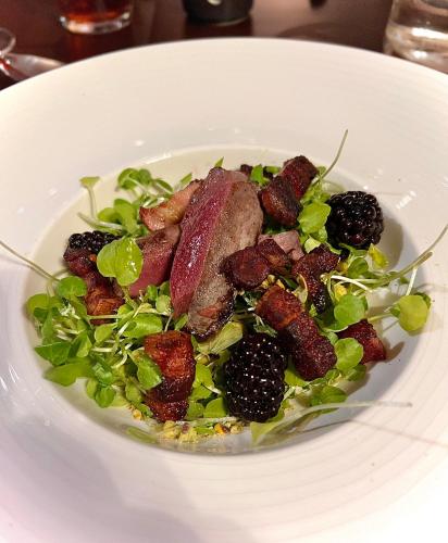 a white plate with a salad with meat and blackberries at The Kings Head in Dorking