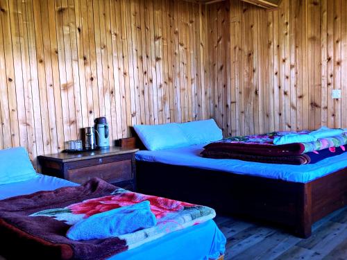 two beds in a room with wooden walls at Phamlhakhang Ecohomestay in Pelling