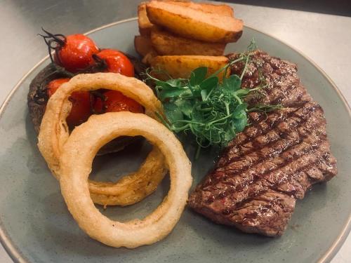 a plate of food with steak and onion rings and tomatoes at The Crossroads Inn in Halifax