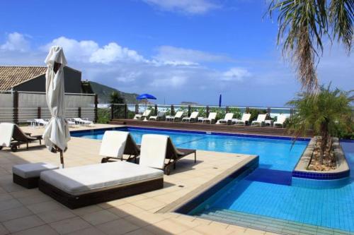 uma piscina com cadeiras e guarda-sóis num resort em Apartamento Costão das Gaivotas - Praia do Santinho - Ingleses - Florianópolis em Florianópolis