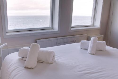 a bedroom with a bed with white sheets and two windows at Fisherman's Cottage in Cockenzie