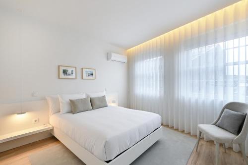 a white bedroom with a white bed and a chair at Casa da Boavista By Sé Apartamentos in Braga