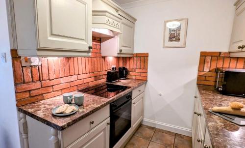 La cuisine est équipée de placards blancs et d'un four avec plaques de cuisson. dans l'établissement Martha's Cottage, à Ironbridge