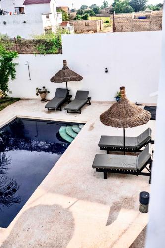 a pool with chairs and umbrellas next to a swimming pool at La Baraka, extravagant villa for 8 with pool in Saly in Gandigal