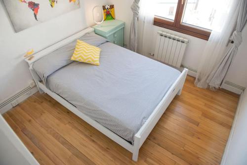 Cama blanca con almohada amarilla en el suelo de madera en Apartamento acogedor en pleno corazón de Urdaibai, en Guernica y Luno