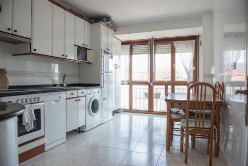 cocina con armarios blancos, mesa y sillas en Apartamento acogedor en pleno corazón de Urdaibai, en Guernica y Luno