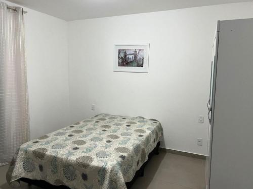 Cama en habitación blanca con una foto en la pared en Apartamento com piscina 15 mim da Praia, en Cabo Frío