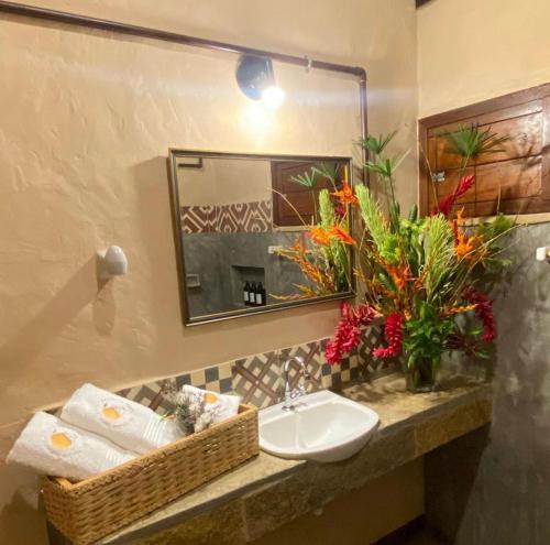 a bathroom with a sink and a mirror and flowers at Quinta dos Laranjais Chalés in Viçosa do Ceará