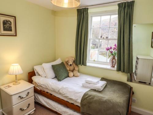 um pequeno quarto com um urso de peluche sentado numa cama em Pavement End Cottage em Grasmere