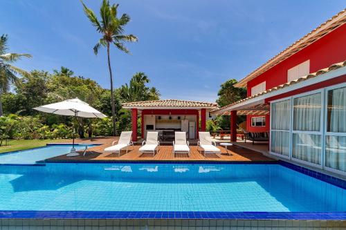 a swimming pool with chairs and an umbrella next to a house at Quintas de Sauípe - Casa D13 in Costa do Sauipe