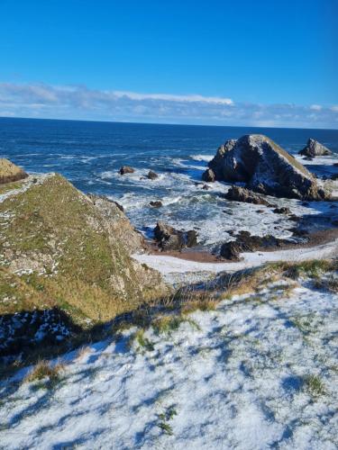a beach with snow on the rocks and the ocean at Victoria Hotel in Portknockie