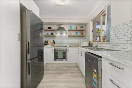 a kitchen with white cabinets and a stainless steel refrigerator at Irrilassa by the Beach by Experience Jervis Bay in Huskisson