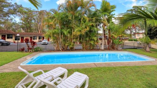 a swimming pool with two white chairs and a house at Kempsey Powerhouse Motel in Kempsey